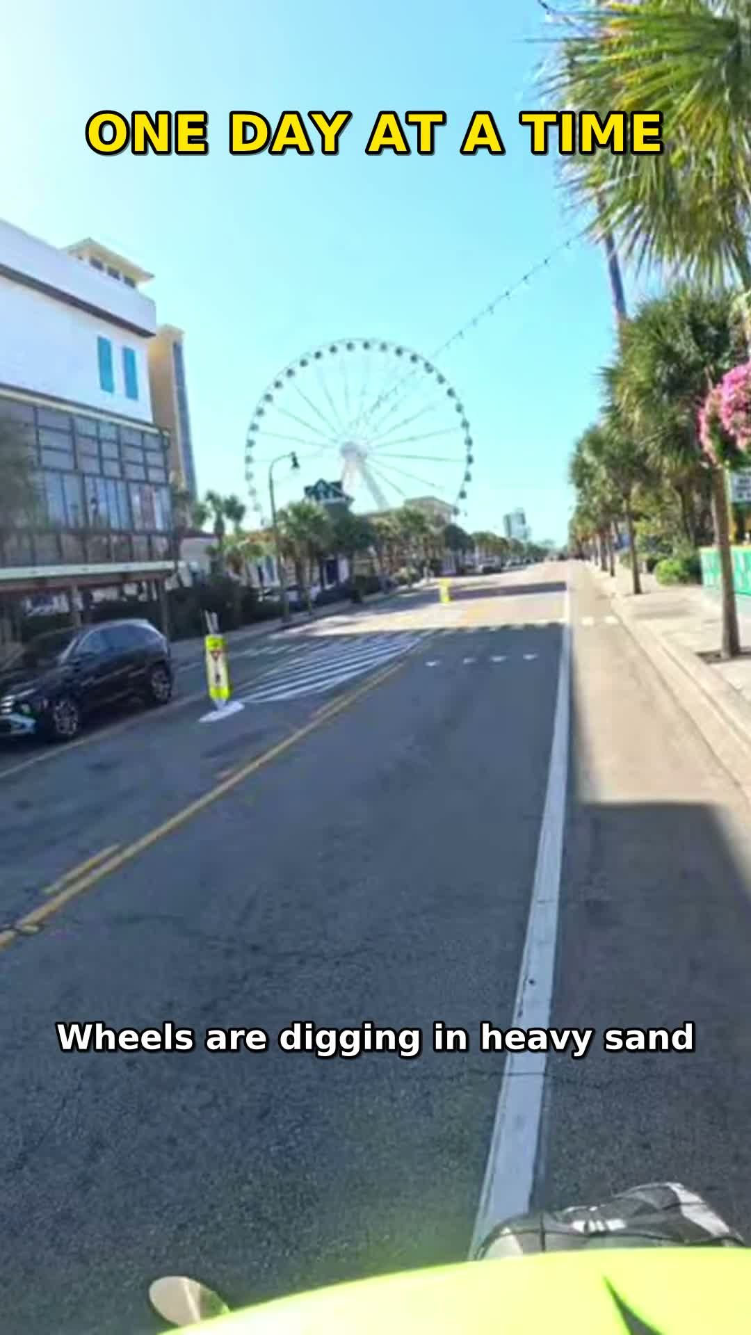 Real photo — enhanced: frame from Coach RODA's ride video — the Myrtle Beach SkyWheel seen from the handlebars on the coastal road